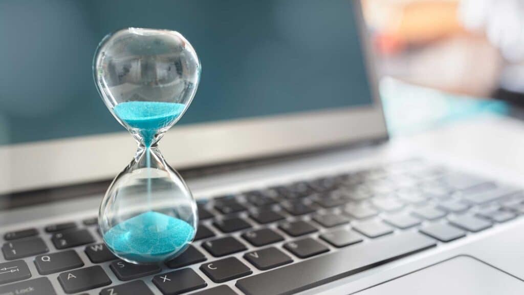 Hourglass with turquoise sand on a laptop keyboard